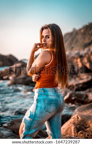 A pretty brunette with a red shirt in a photo shoot on a sunset on some rocks