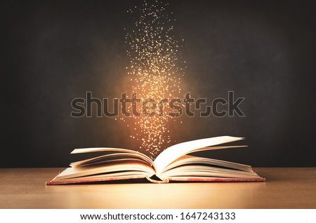 An old, worn, red text book, lying opened on a classroom desk with sparkles and stars rising upwards from its centre. Black chalkboard background. Royalty-Free Stock Photo #1647243133