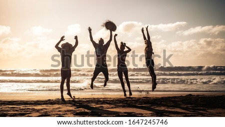 Happy people jump with joy and happiness during summer holiday vacation together in friendship having fun - silhouettes young couples at the beach