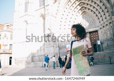 Attractive dark skinned traveler with paper map enjoying city sightseeing around ancient heritage of touristic urbanity, young female photographer exploring world during summer vacations for recreate Royalty-Free Stock Photo #1647246949