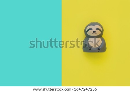 Flat lay antistress toy squish gray sloth with mouth, eyes, nose. Bright yellow and blue background.Compressing, soft, squeezable items to relieve stress, problems, anxieties, worries.Summer concept.