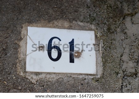 Old number tag on the wall of an house with "61" written on it