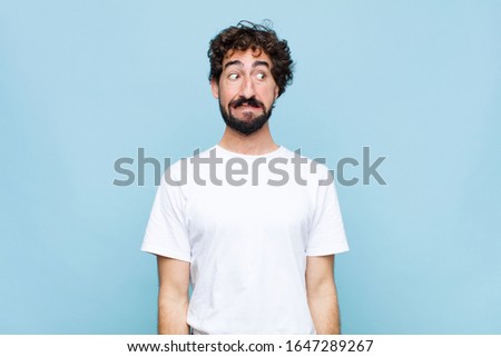 young crazy bearded man looking worried, stressed, anxious and scared, panicking and clenching teeth against flat wall