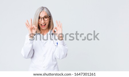 middle age doctor woman feeling shocked, amazed and surprised, showing approval making okay sign with both hands