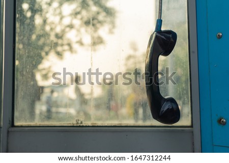 Telephone receiver hanging in phone booth Royalty-Free Stock Photo #1647312244