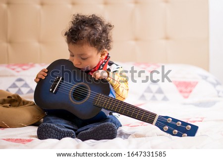 A little boy, boy, children with a cowboy hat or a woody toy story costume, playing with a blue guitar Royalty-Free Stock Photo #1647331585