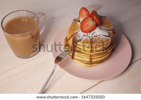 Late breakfast or dinner with lush pancakes sprinkled with powdered sugar, strawberries and tea in a glass mug on a light wooden background