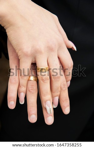 Close-up cropped picture of hands of bride and groom with gold wedding rings on them on dark background. Beautiful wedding manicure. Idea for wedding manicure.