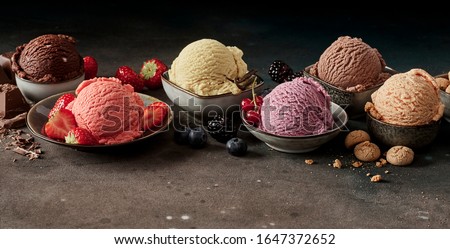 Scopes of various flavour ice cream in small bowls, served with berries and other ingredients, viewed in close-up on dark table. Professional studio shot