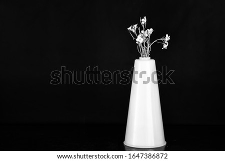 A small bouquet of flowers in a white vase, black and white