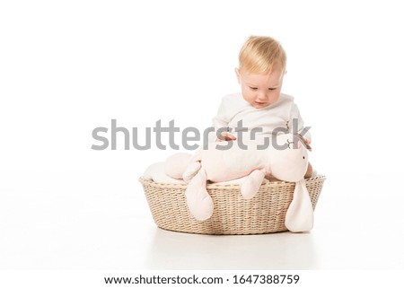 Child looking at pink bunny and sitting on blanket in basket on white background