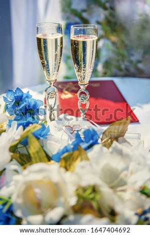 Vertical picture of wedding glasses with champagne, bride and groom rings and wedding decorations in summer sunny wedding day. Wedding and happiness concept