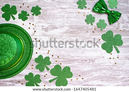 Happy Saint Patrick's Day greeting card with traditional symbols, shamrock, green attire. Green hat, bow tie, St Patricks Day shamrocks, golden confetti on white wooden background, copy space