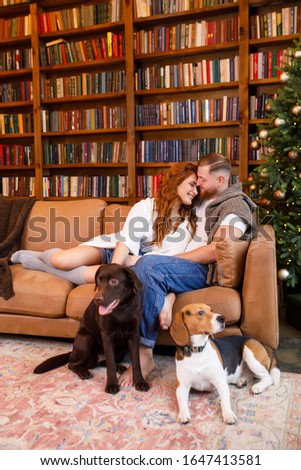 young beautiful couple sitting on the bed with two dogs on the background of the library and books in the apartment in the loft style