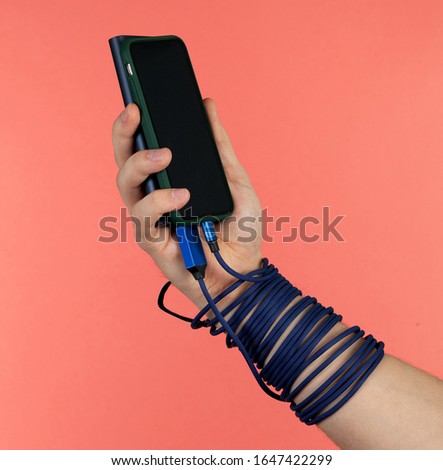 Hand holds phone with powerbank charging blue cable on pink background.
