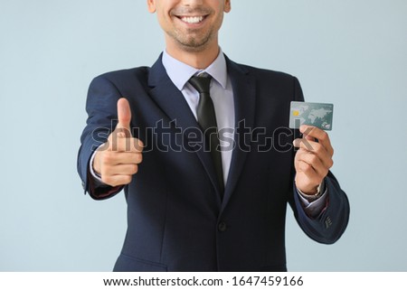 Male bank manager with credit card showing thumb-up gesture on light background