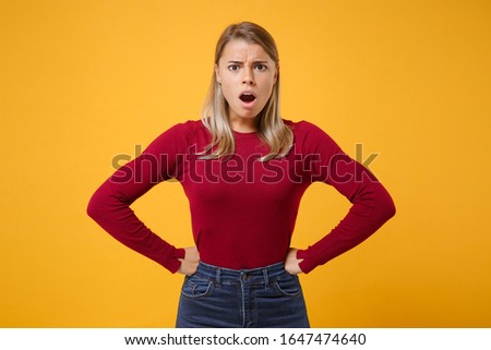Shocked irritated young blonde woman in casual clothes posing isolated on yellow orange background studio portrait. People lifestyle concept. Mock up copy space. Standing with arms akimbo on waist
