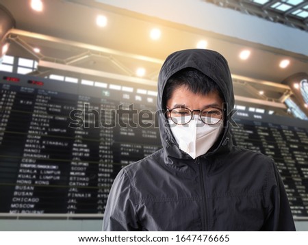 Asian man wearing surgical mask to prevent flu disease Coronavirus with blurred image of airport flight time table