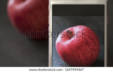 A picture of cell-phone screen while it focuses on a red apple lying in front of it on a grey table