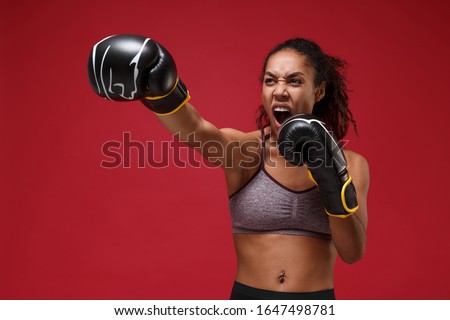 Screaming young african american sports fitness boxer woman in sportswear working out isolated on red wall background. Sport exercise healthy lifestyle concept. Make boxing exercises in boxing gloves