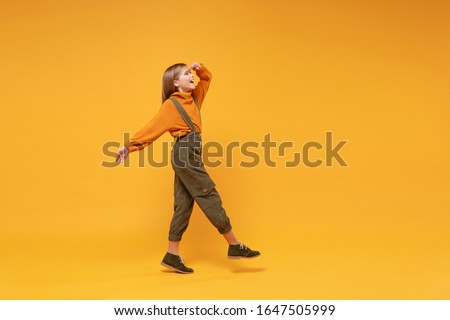Side view of little kid girl 12-13 years old in turtleneck, jumpsuit isolated on yellow background. Childhood lifestyle concept. Mock up copy space. Holding hand at forehead looking far away distance Royalty-Free Stock Photo #1647505999