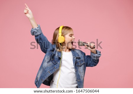 Cute little kid girl 12-13 years old isolated on pastel pink background. Childhood lifestyle concept. Mock up copy space. Listen music with headphones sing song in microphone pointing index finger up Royalty-Free Stock Photo #1647506044