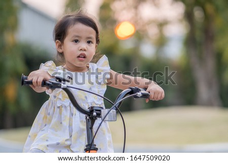 Yellow dressed beautiful little girl riding bicycle at park.