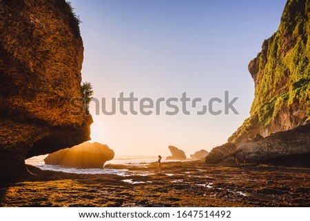 Traveller woman in swimsuit posing at sunset near ocean and rocks in Bali. Woman in bikini and amazing landscape