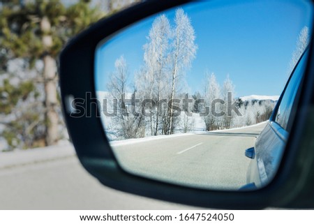 Driveway Snow-covered Birch Forest on a beautiful sunny Day seen in a Car Side Mirror