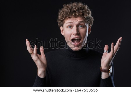 Excited young man wearing turtleneck standing isolated infront of a black background, looking at camera