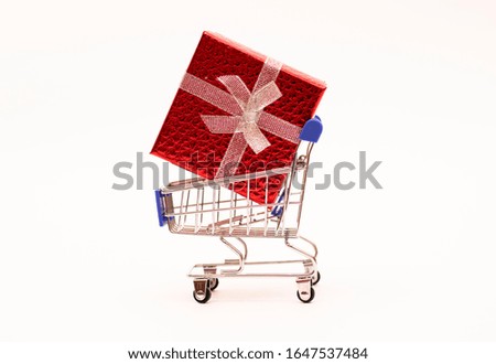 a gift in a red box tied with a banot rides in a metal trolley on wheels on white background