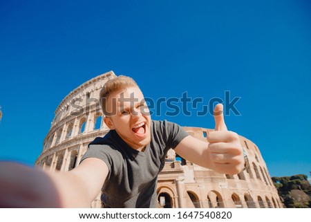 Happy young man making selfie thumb up sign in front of Colosseum in Rome, Italy. Concept travel trip.
