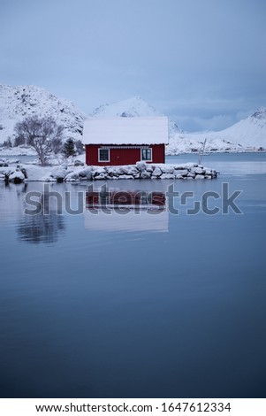 Winter picture of typical red remote norwegian house by the sea with a beautiful view to the mountains. Located in small town Ballstad in Lofoten Islands. 
