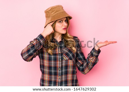 Young caucasian woman wearing a hat isolated holding and showing a product on hand.