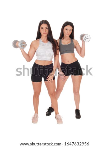 Two young beautiful woman standing in workout outfits in the studio
working out with there dumbbells, isolated for white background
