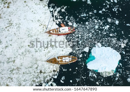drone view photo of two yachts staying on ice anchor and one huge iceberg