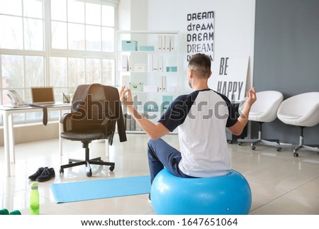 Man meditating on fitness ball in office