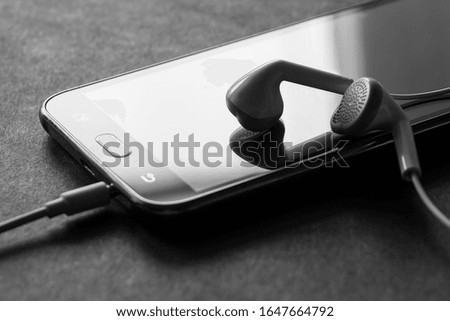 Headphones and smartphone on a dark gray background. Stylish black and white photo.