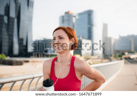 Young woman runner with water bottle in city, resting. Copy space.