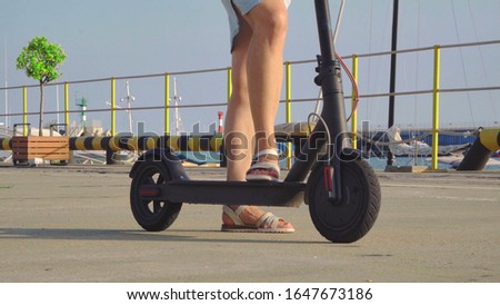 A woman on the street is standing on an electric scooter. Women's feet on an electric scooter.