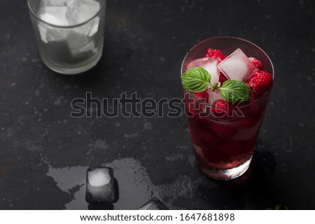Raspberry alcoholic cocktail with liqueur, vodka, ice and mint on a dark background. Raspberry Mojito. Refreshing cool drink, lemonade or ice tea in a glass. Close up, 