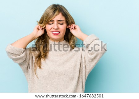 Young blonde caucasian woman covering ears with fingers, stressed and desperate by a loudly ambient.