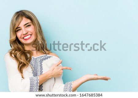 Young blonde caucasian woman excited holding a copy space on palm.