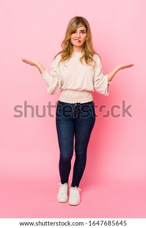 Young blonde caucasian woman standing over a pink background confused and doubtful shrugging shoulders to hold a copy space.