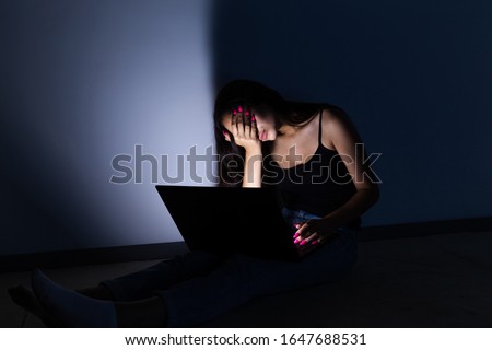 sad and female teenager with tablet computer and laptop suffering cyberbullying and harassment being online abused by stalker or gossip feeling desperate and humiliated in cyber bullying. Royalty-Free Stock Photo #1647688531