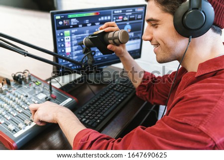 Image of young happy caucasian dj man wearing headphones working at radio station while making podcast recording for online show