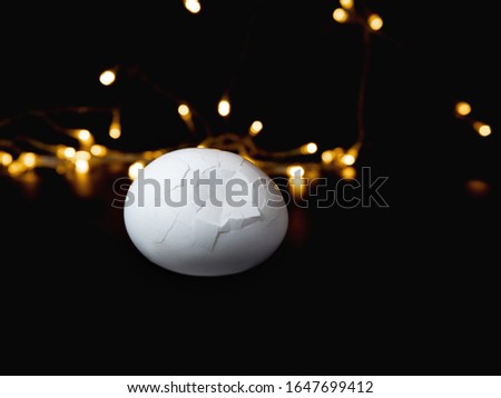 a broken white egg all in cracks on a black background and yellow bokeh
