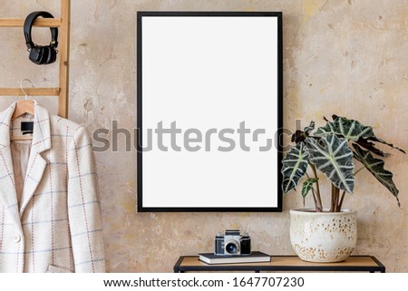 Modern composition of living room interior with black mock up poster frame, photo camera, plant, wooden ladder, jacket and elegant personal accessories. Stylish home decor. Grunge wall. Template.