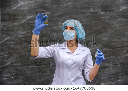 Chemist examining test tube with substance. She's in protective uniform over grey abstract grey background