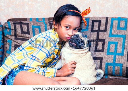 Cute little indian girl playing with her pet dog pug inside home